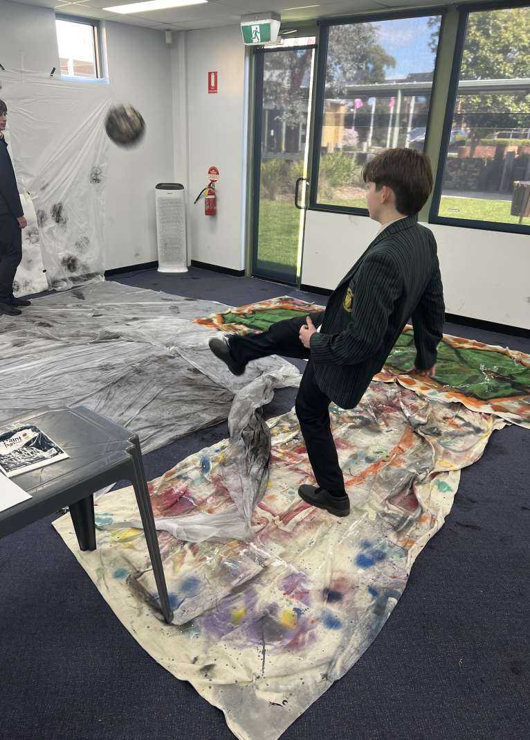 Students kicking a football covered in paint to create a piece of artwork for Art week